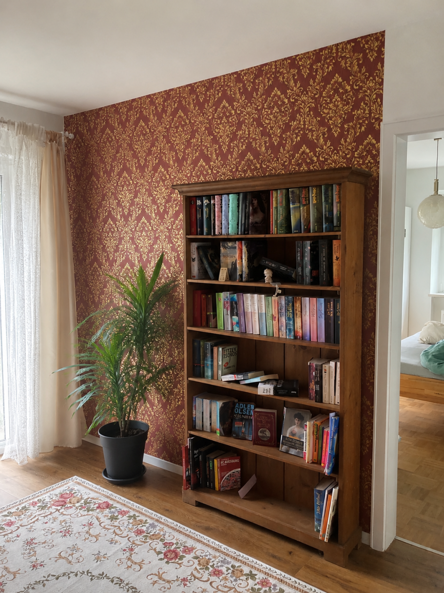 Textiltapete Ein Bücherregal mit verschiedenen Büchern neben einer grünen Pflanze und einer gemusterten Wand.