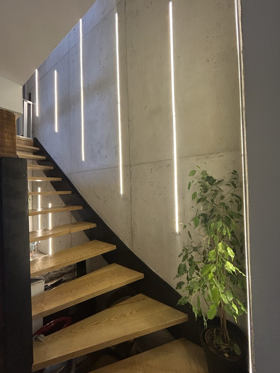 Betonoptik Helle Treppe mit Holzstufen, Wänden aus Beton und schmalen, vertikalen Lichtern.