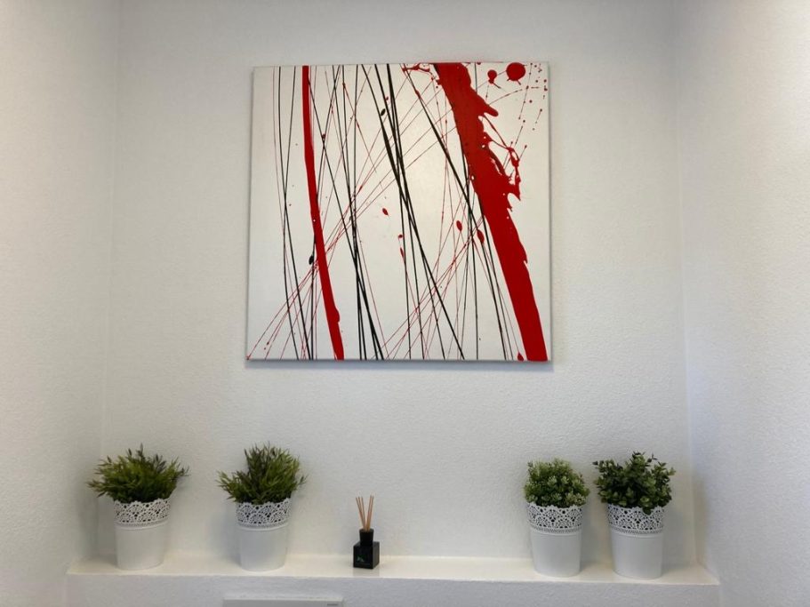 Abstrakte Wandkunst Abstrakte Wandkunst mit roten Linien und Spritzern, umgeben von Pflanzen in Töpfen.